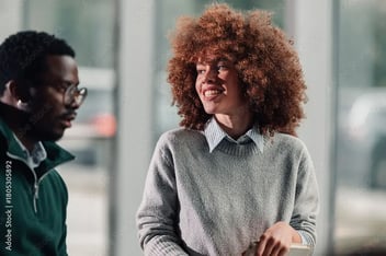 Mulher sorrindo e conversando com um homem em um ambiente interno claro.
